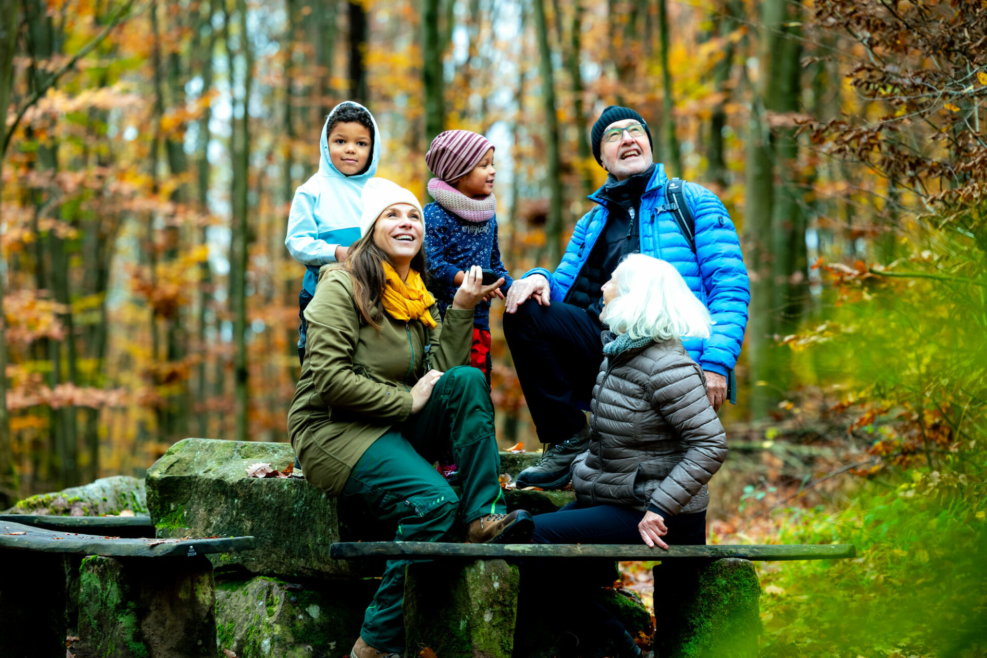Familie sitzt im Wald auf einer Bank und hört sich die Audiotour an