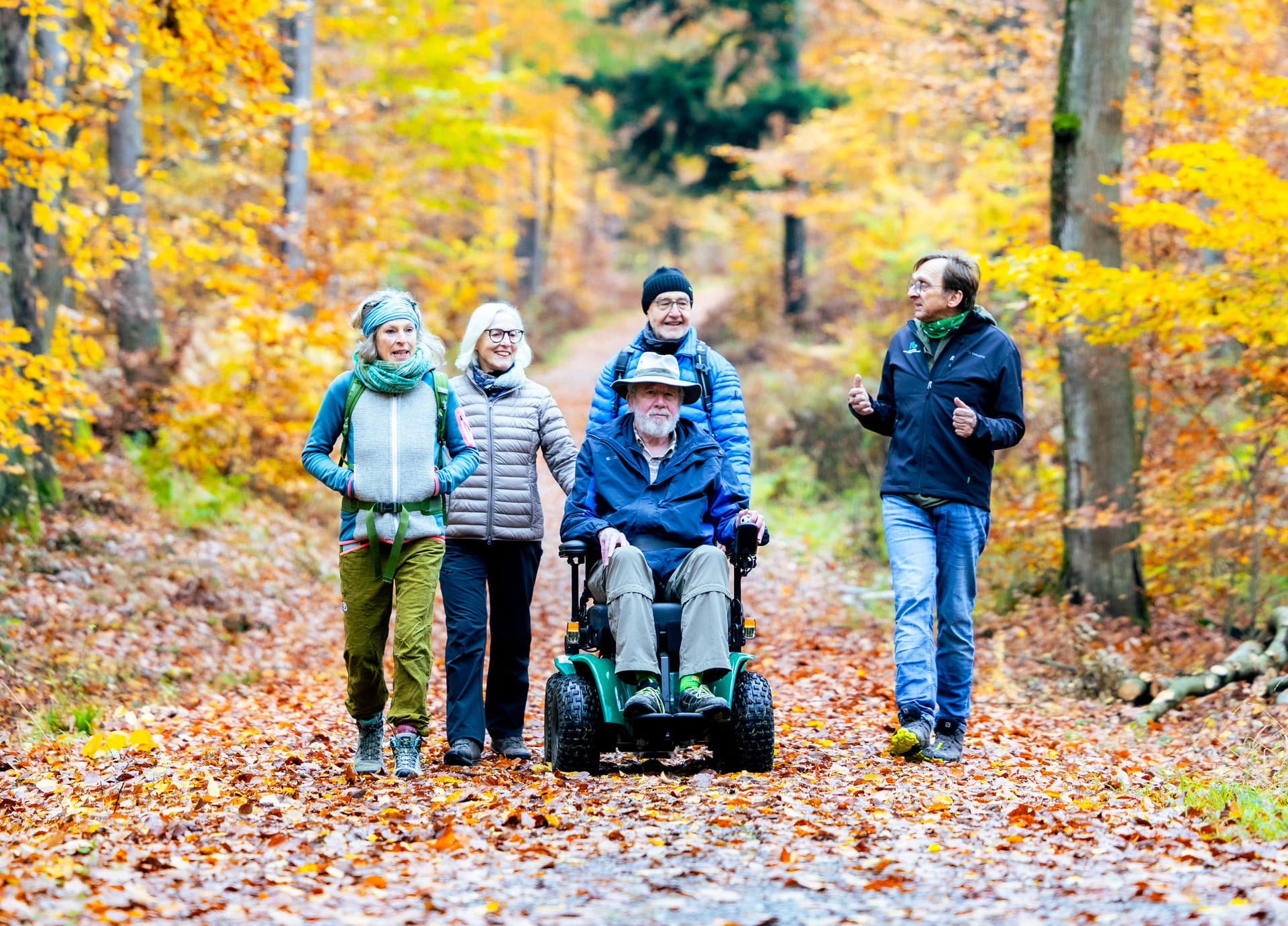 Gruppe von Menschen mit einem älteren Herren im Outdoor-Rollstuhl im Herbstwald