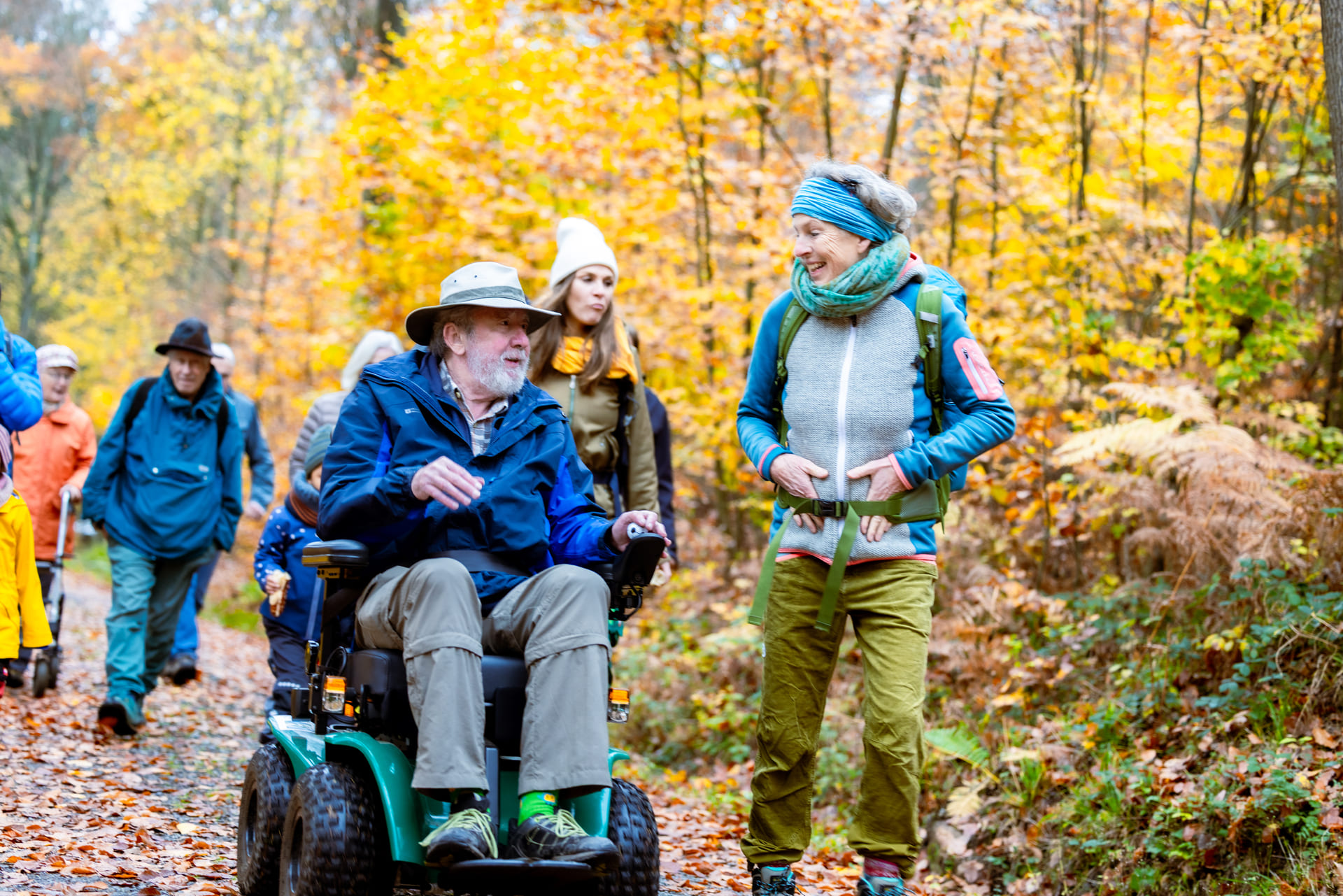 Gruppe von Menschen mit einem älteren Herren im Outdoor-Rollstuhl im Herbstwald