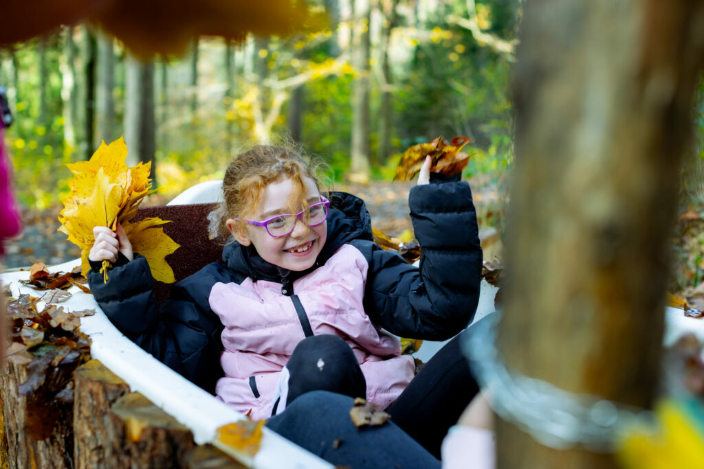 Fröhliches Mädchen in einer Waldbadewanne mit Herbstlaub