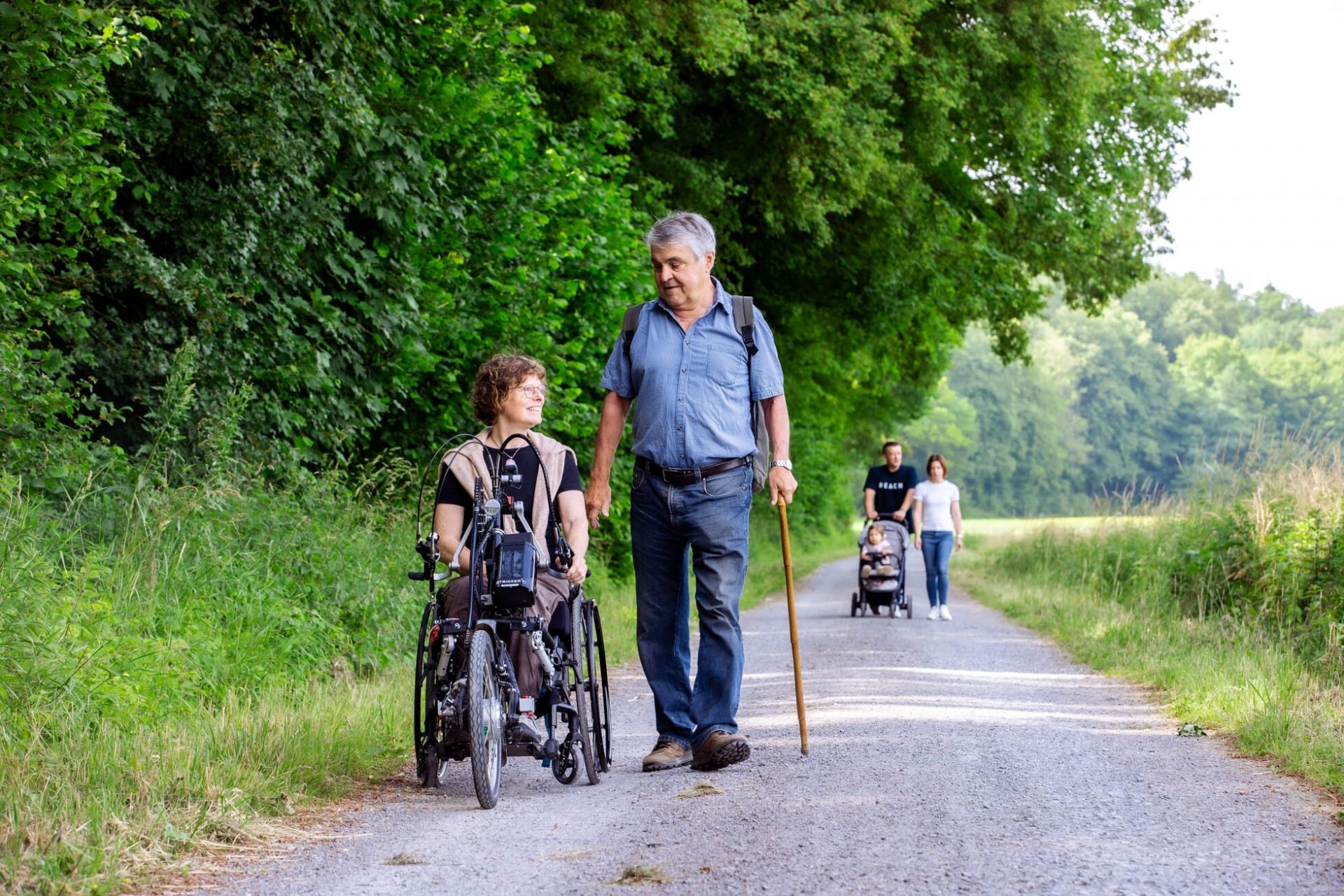 Frau im Rollstuhl ist mit wanderndem Mann auf einem Komfort-Wanderweg im Naturpark unterwegs
