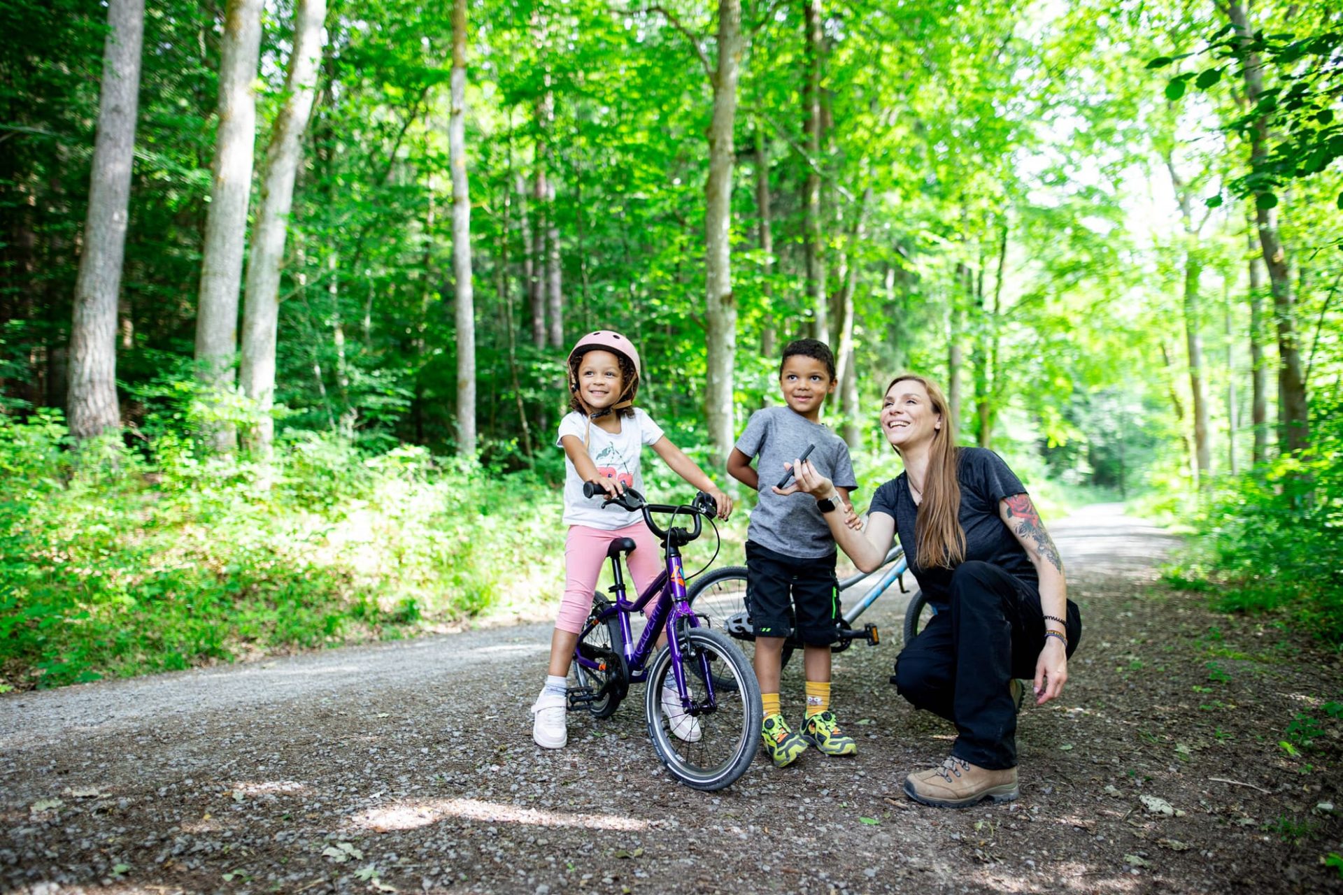 Eine Frau mit ihren beiden Kindern sind im Wald und lauschen gemeinsam einer Kinder-Audiotour.
